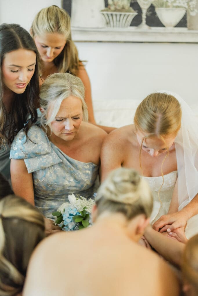 Bridesmaids and mother praying over bride before ceremony