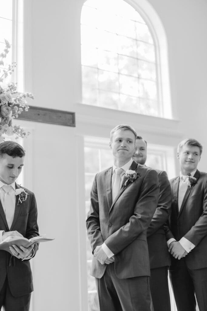 Groom reaction to bride walking down the aisle in white chapel ceremony