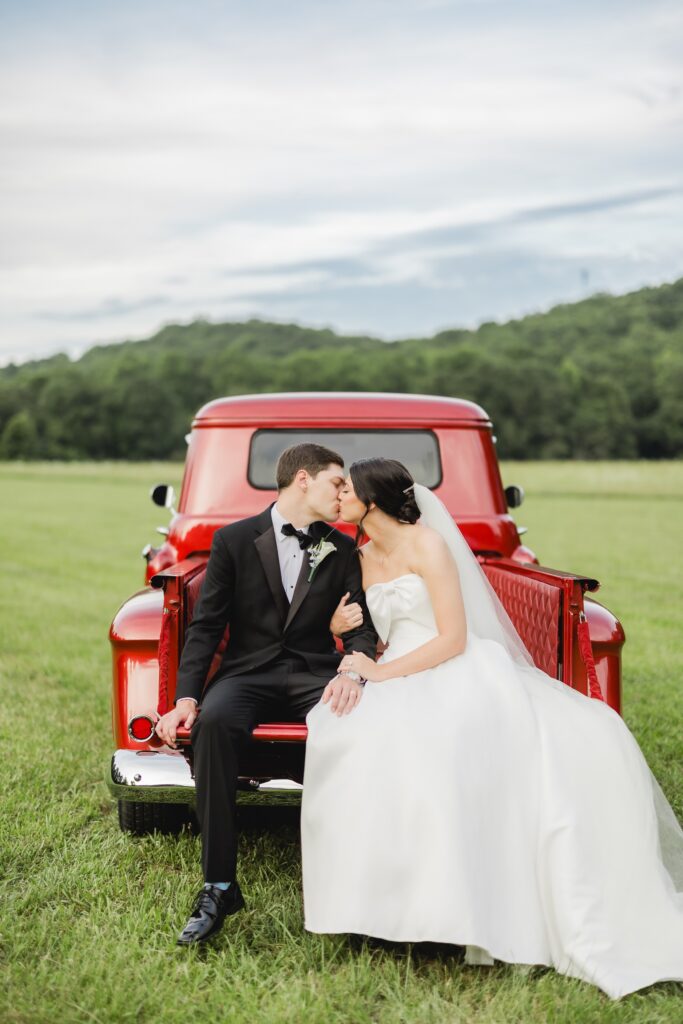Abby and Jonathan sitting together in a vintage red pickup truck during sunset portraits.